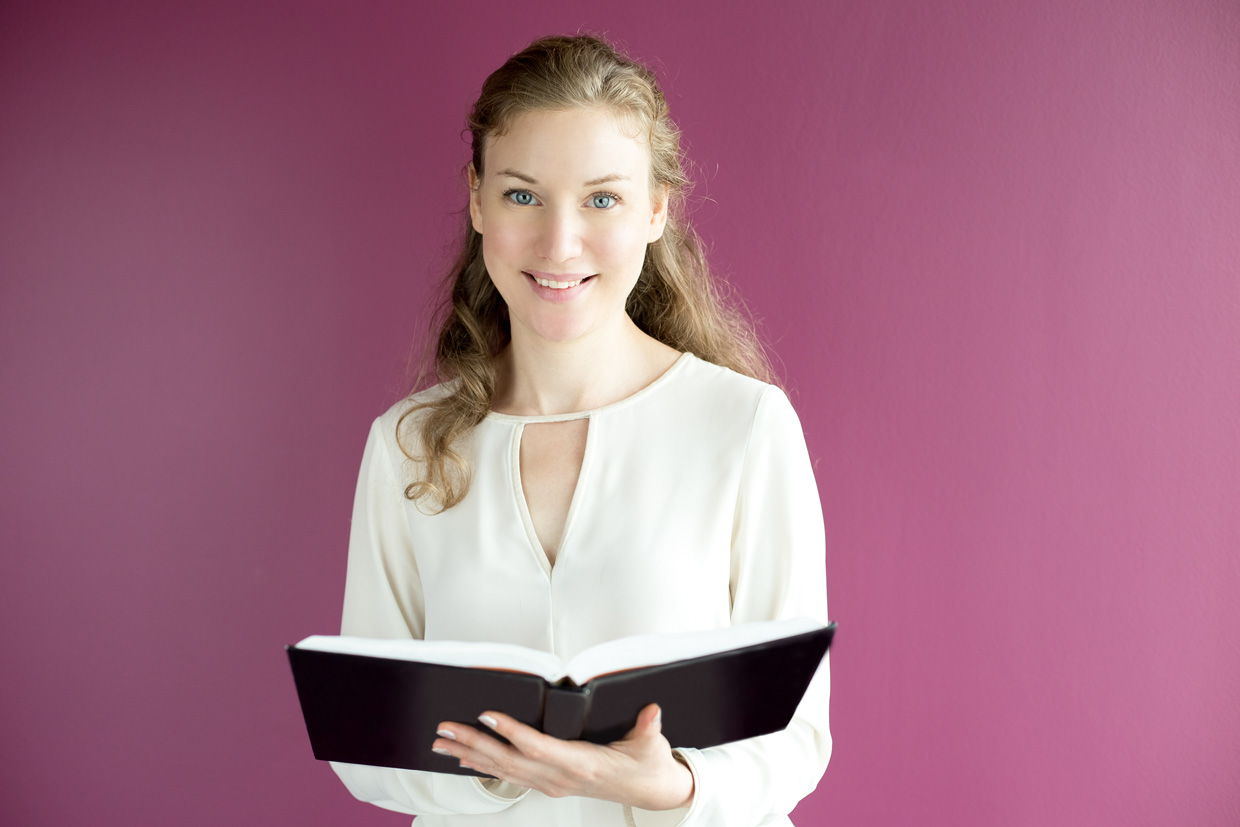 Fotografia apresenta um retrato de uma mulher segurando um livro aberto à sua frente.