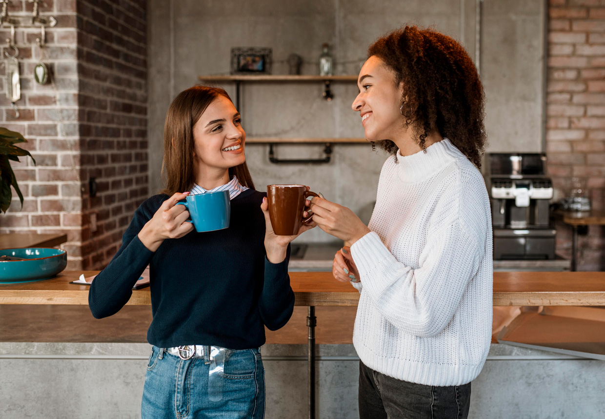 Fotografia apresenta duas jovens conversando e tomando café. 